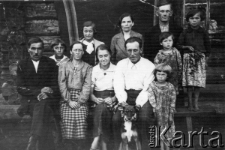 Polscy zesłańcy na Syberii. Grupa ludzi i pies na ławce przed chałupą z bali. Pierwszy od lewej: Michał Niedużak, obok jego żona Anna, za ich plecami starsza córka Janina, obok niej młodsza Stanisława, stoi z tyłu Józef Pułkowski, w białej koszuli Maria Kuźmierczak z d. Pułkowska.