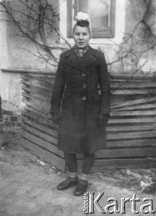 Irena Lewandowska, zaginiona podczas II wojny światowej, na zdjęciu ubrana w palto, półbuty i w chustce na głowie stoi przed budynkiem.