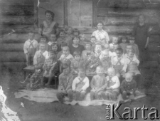 Wychowankowie Domu Dziecka ze swoimi opiekunkami pozują do fotografii siedząc przed ścianą budynku.